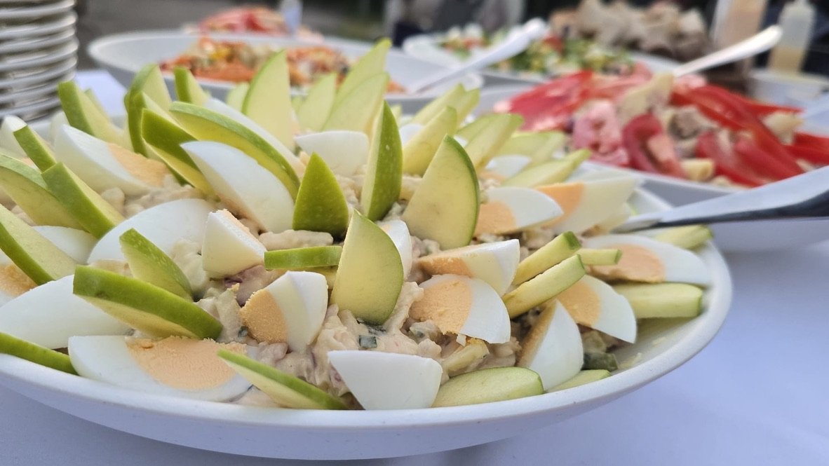 Buffet met een schaal salade met ei en appel, met meer schalen erachter.