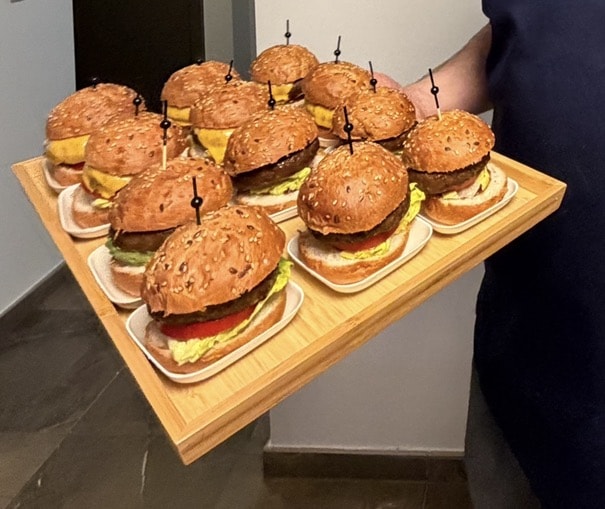 Houten plank met hamburgers, elk met een prikker, die wordt rondgedragen.