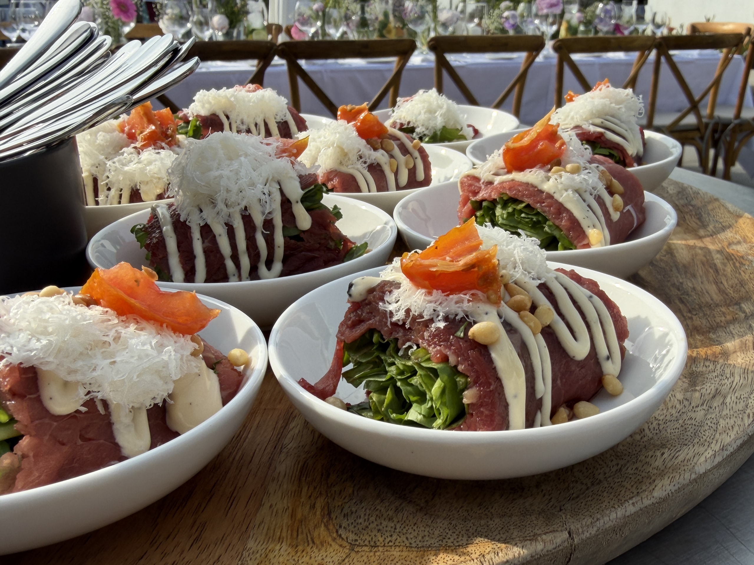 Kommen met opgerolde carpaccio, rucola, mayonaise, pijnboompitten en geraspte kaas.