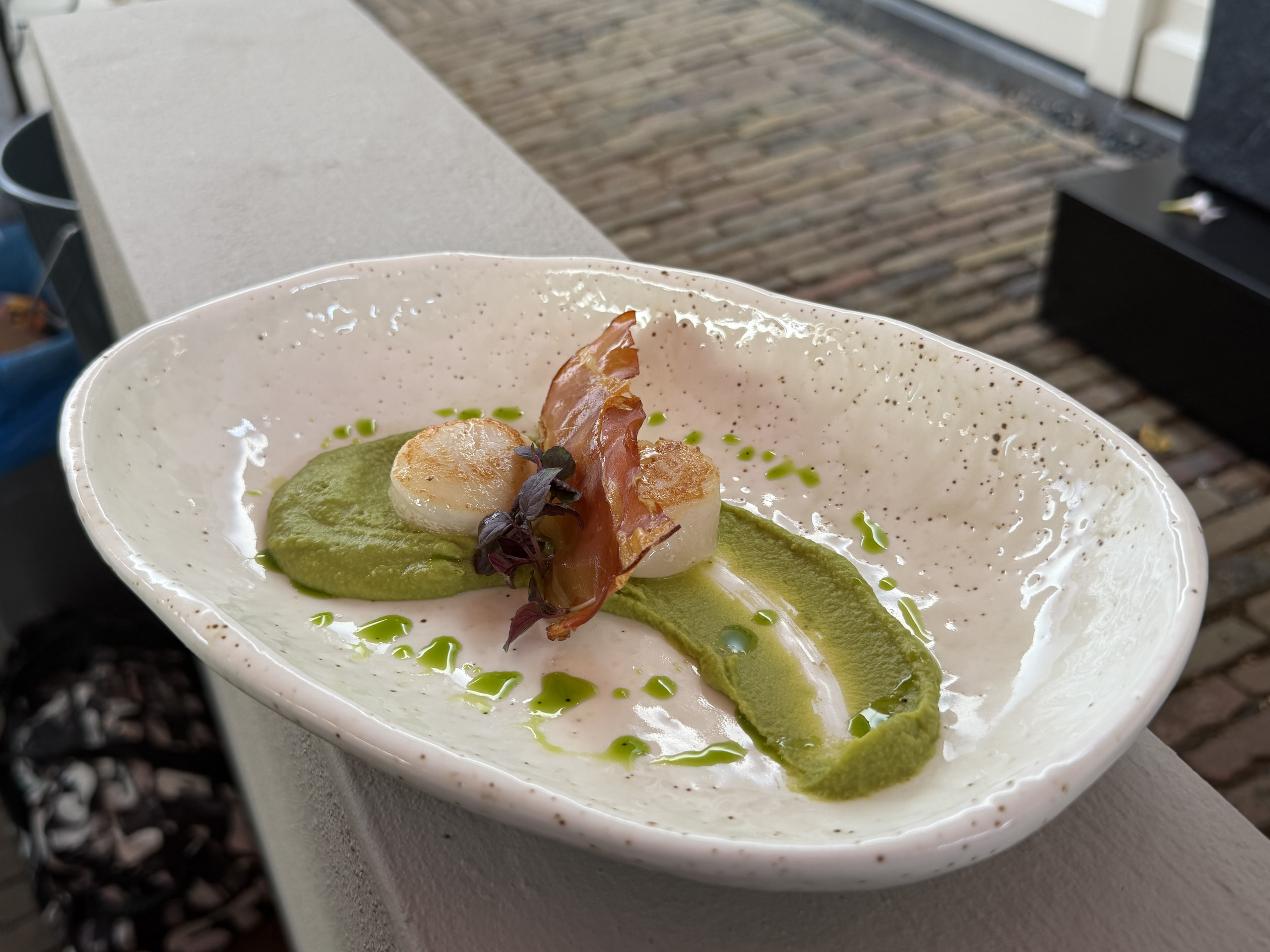 Ovale schaal met coquille, krokante ham en doperwtencrème, buiten gefotografeerd.
