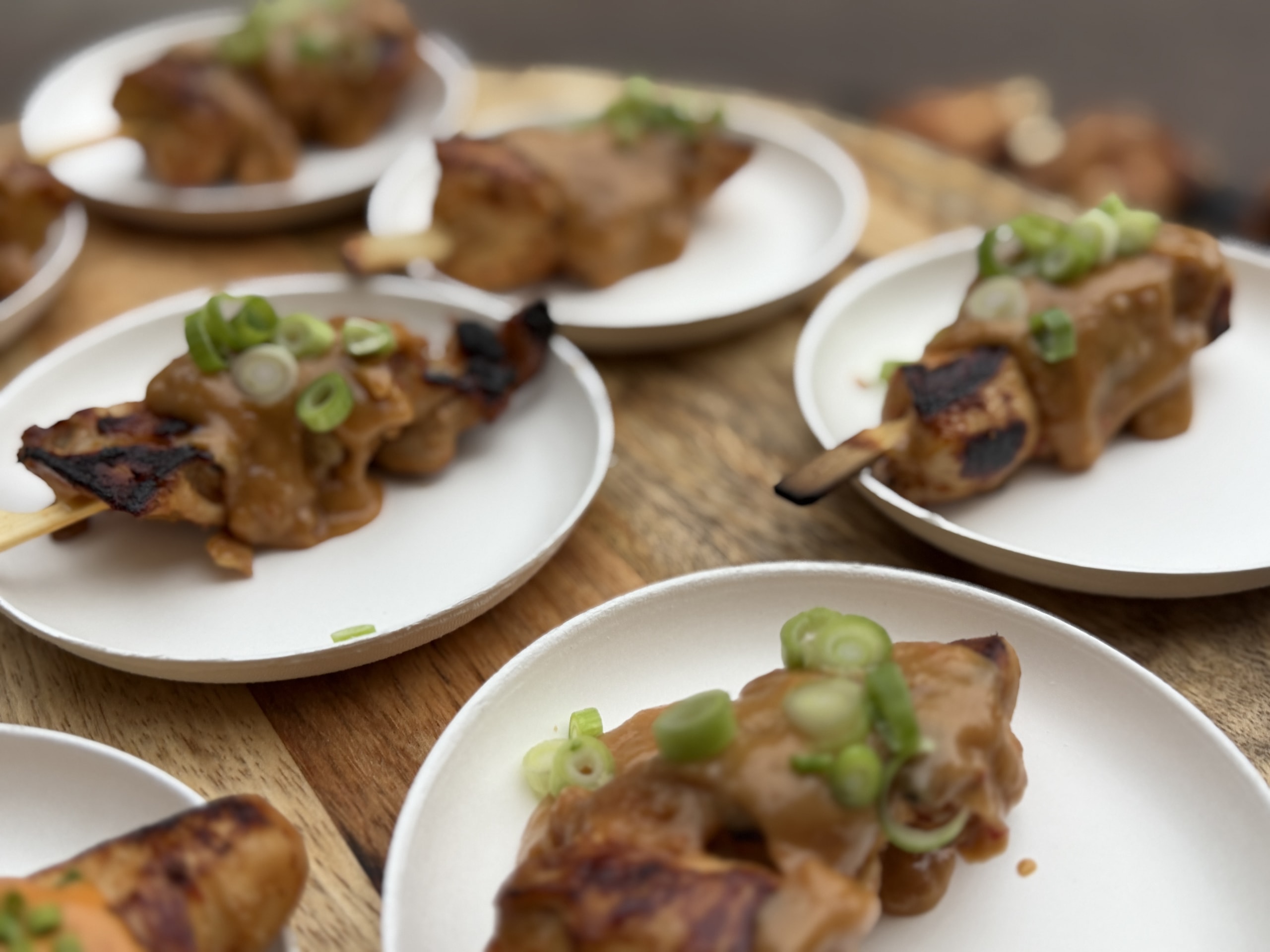 Bordjes met gegrilde spiesjes in satésaus, afgewerkt met lente-ui.