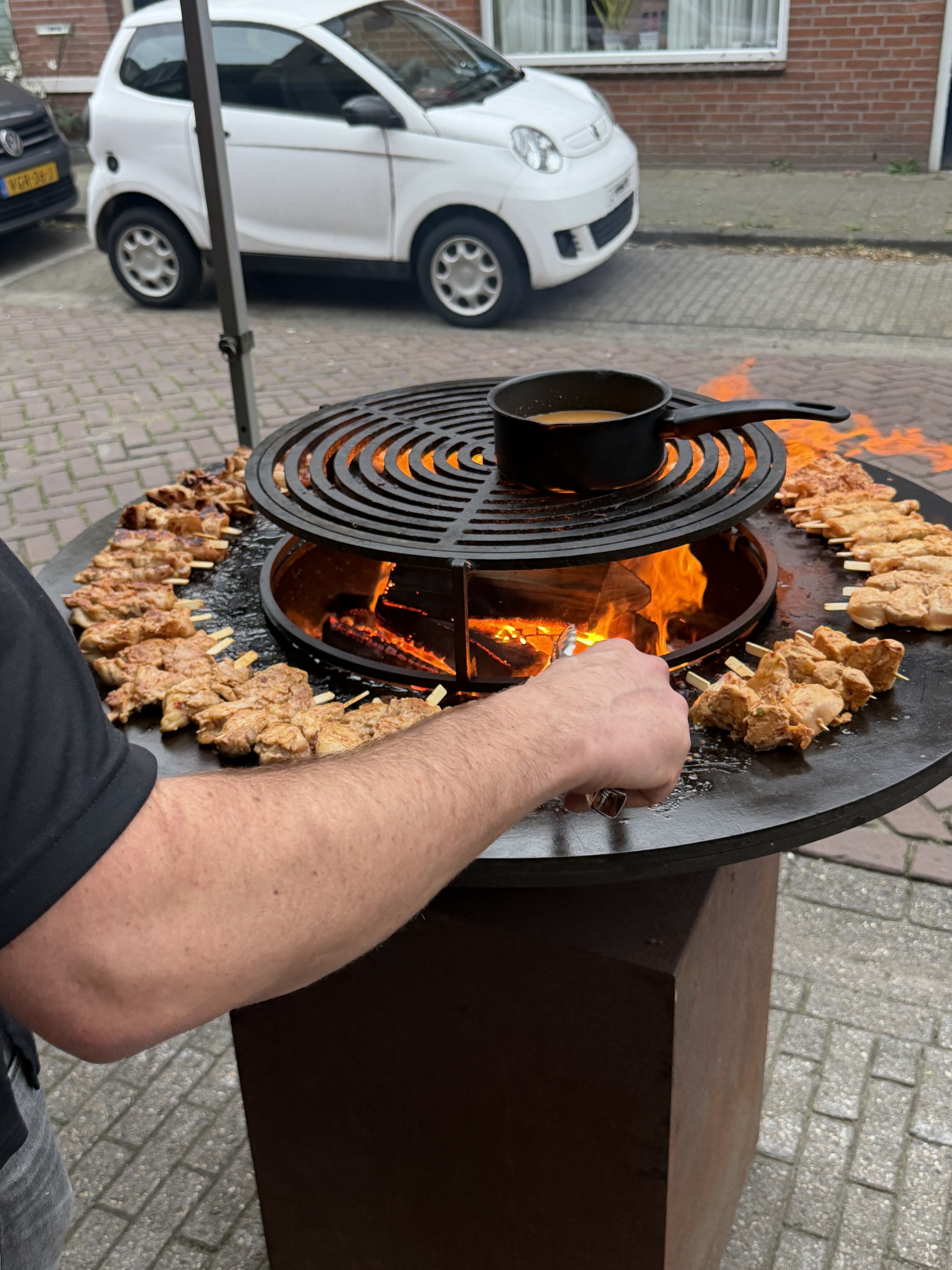 Hand bij de spiesen op een ronde vuurplaat, met open vuur in het midden.