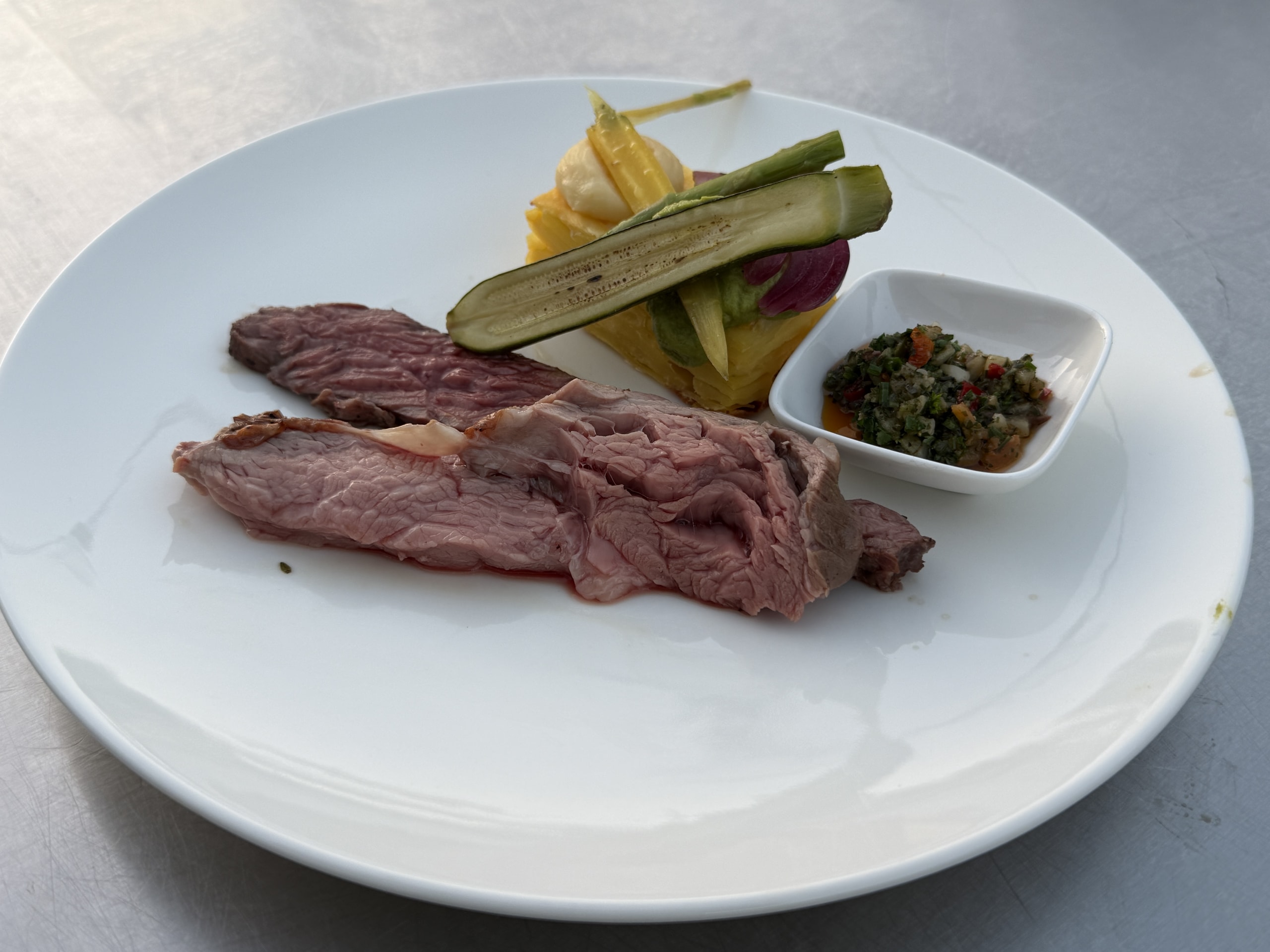 Gesneden steak op een wit bord met gegrilde groente en een bakje kruidensaus.