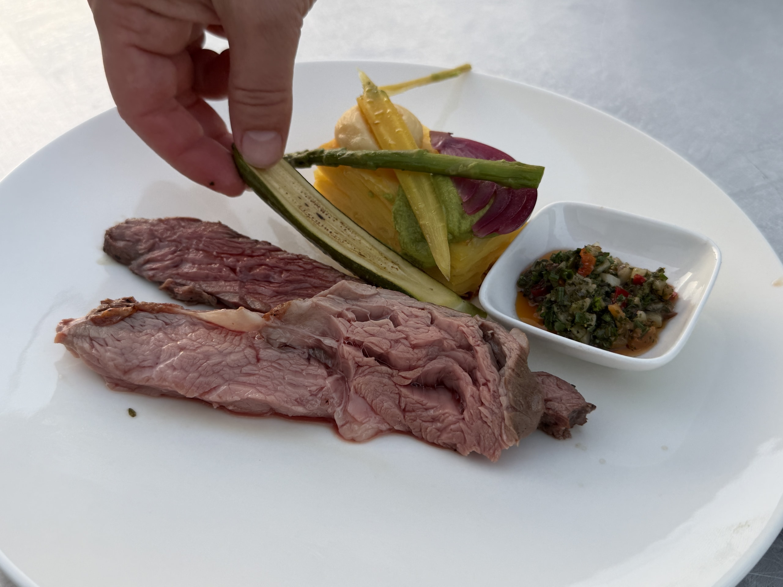 Hand die gegrilde groente op een bord met gesneden steak legt.